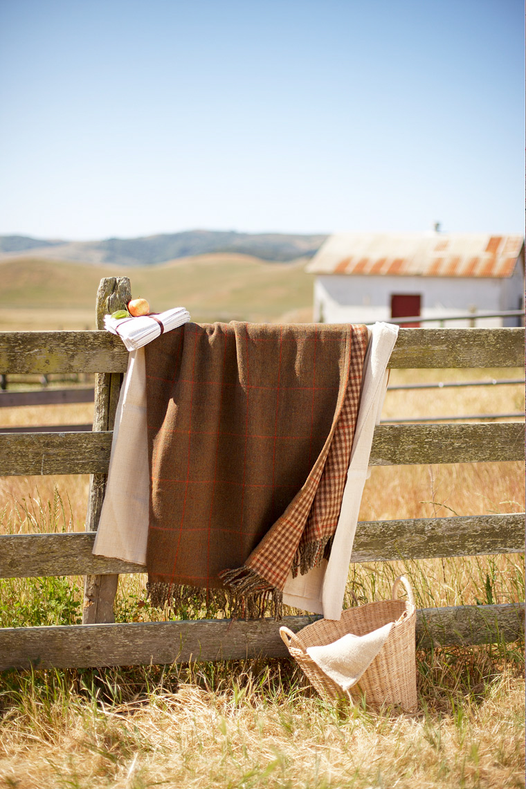 Brown And White Quilts Draped Over Barn Fence With Woven Basket