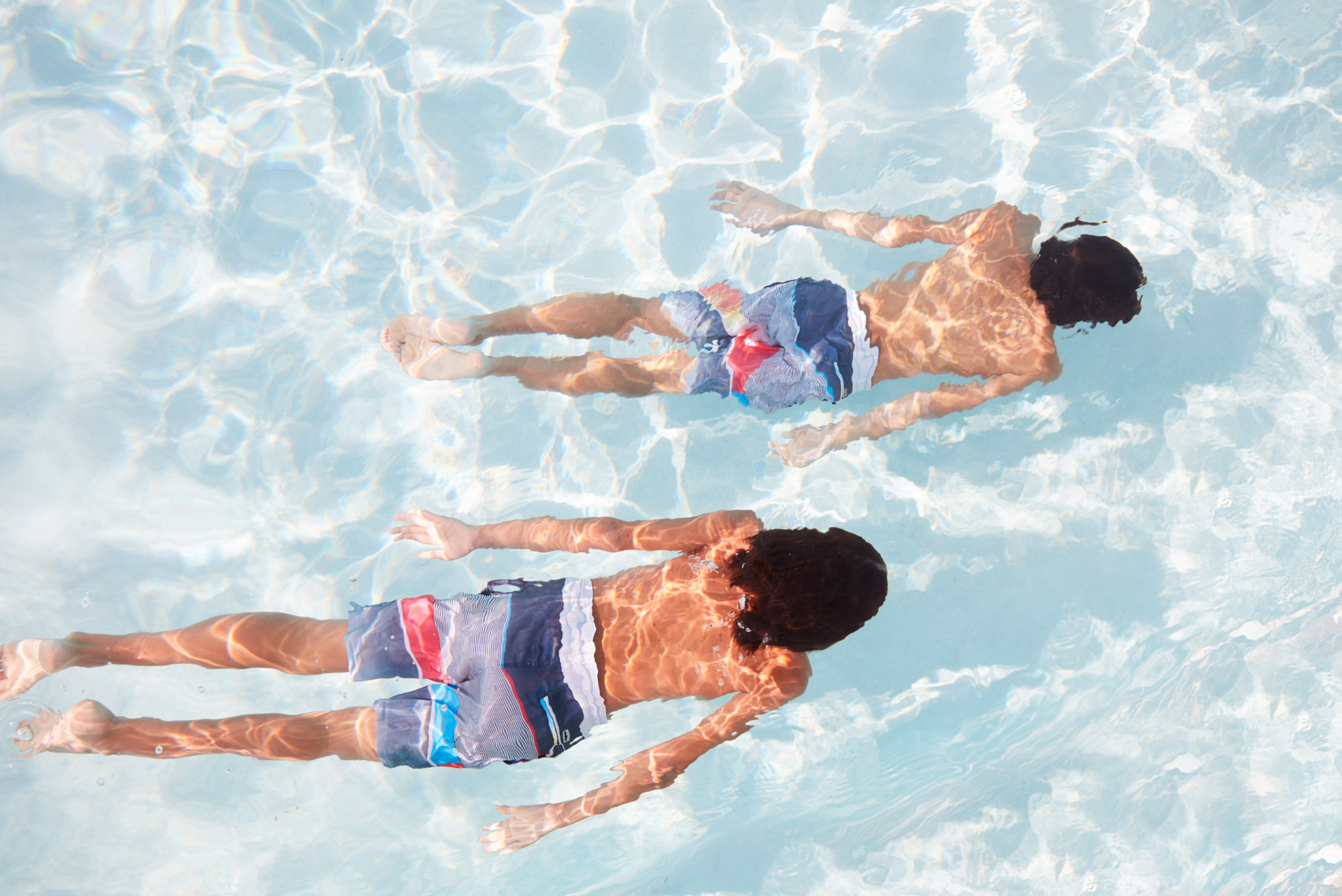 Two boys in colorful bathing suits swimming underwater in clear pool San Francisco lifestyle photographer