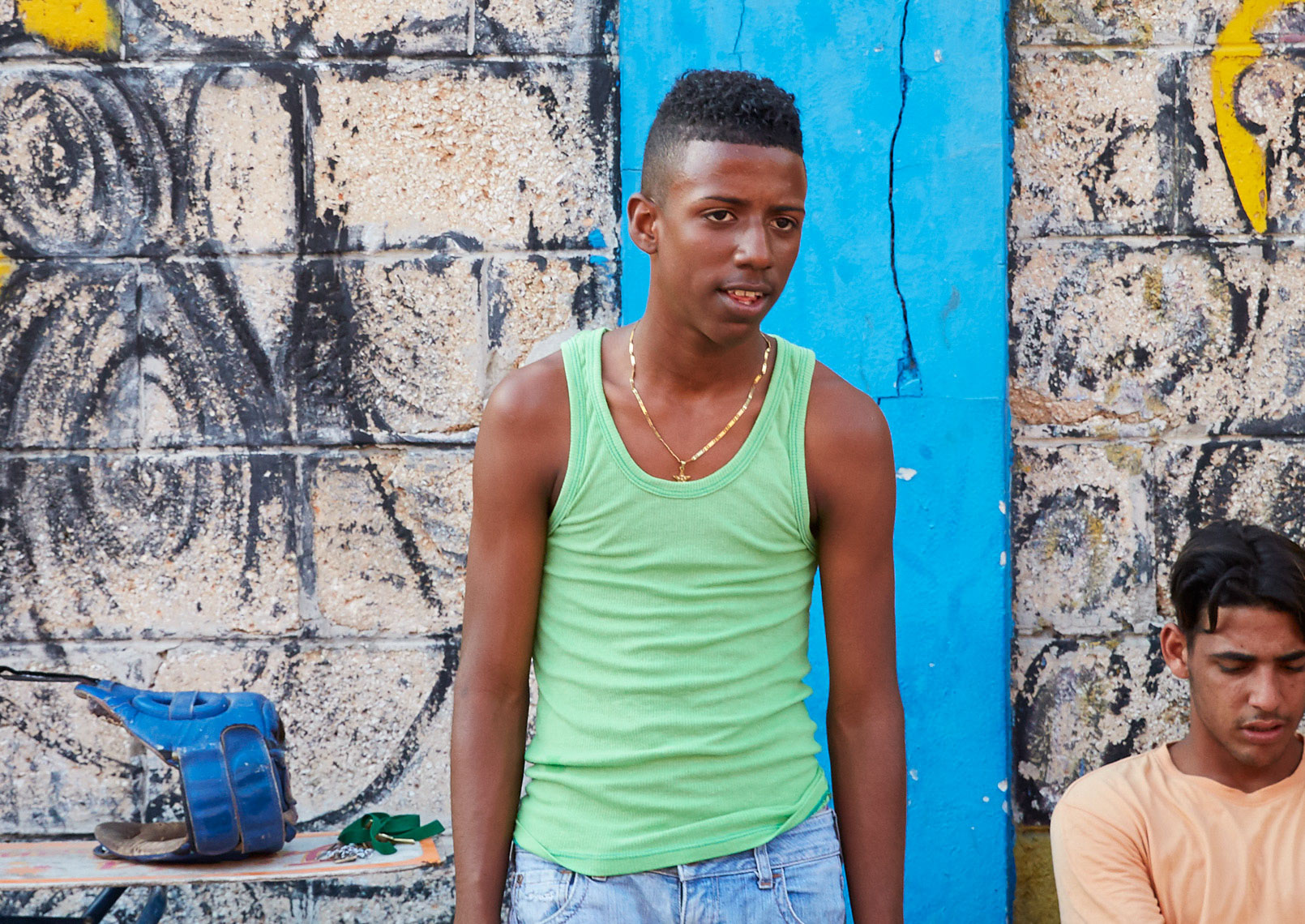 young boy in green shirt and gold chain with blue wall in Cuba