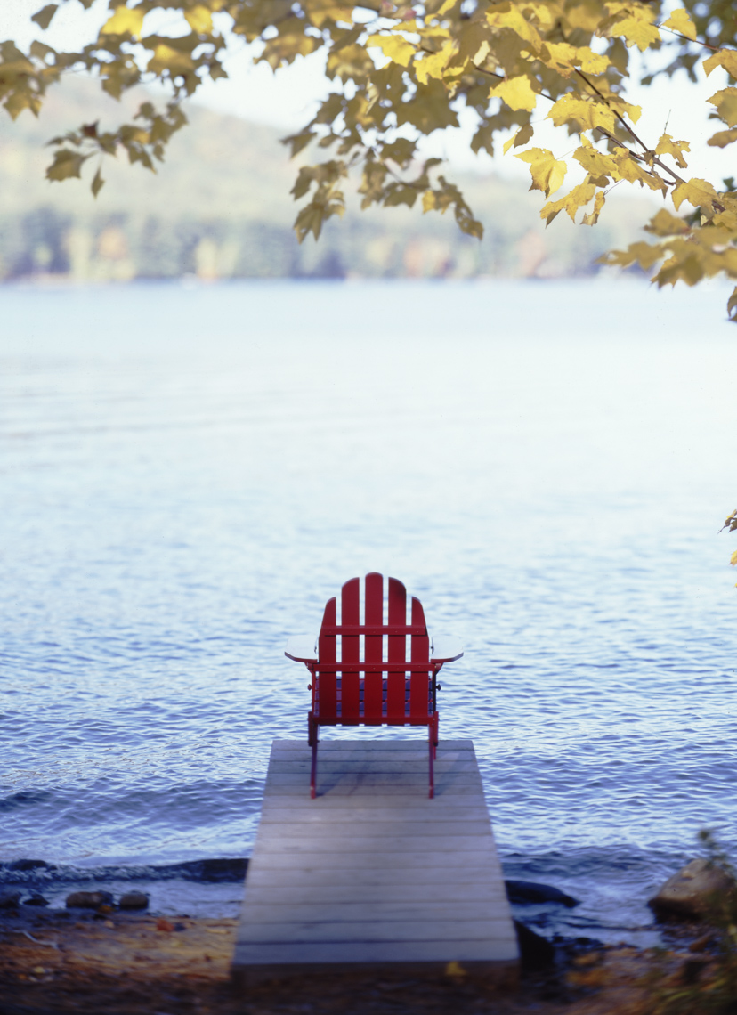 Red Adirondack Chair On Narrow Dock On Lake In Maine